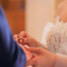 Smile! Diana Kosakowska fotografia - Dłonie Panny Młodej w koronkowej sukni trzymające obrączki ślubne, zbliżenie na delikatne dłonie i złote krążki.