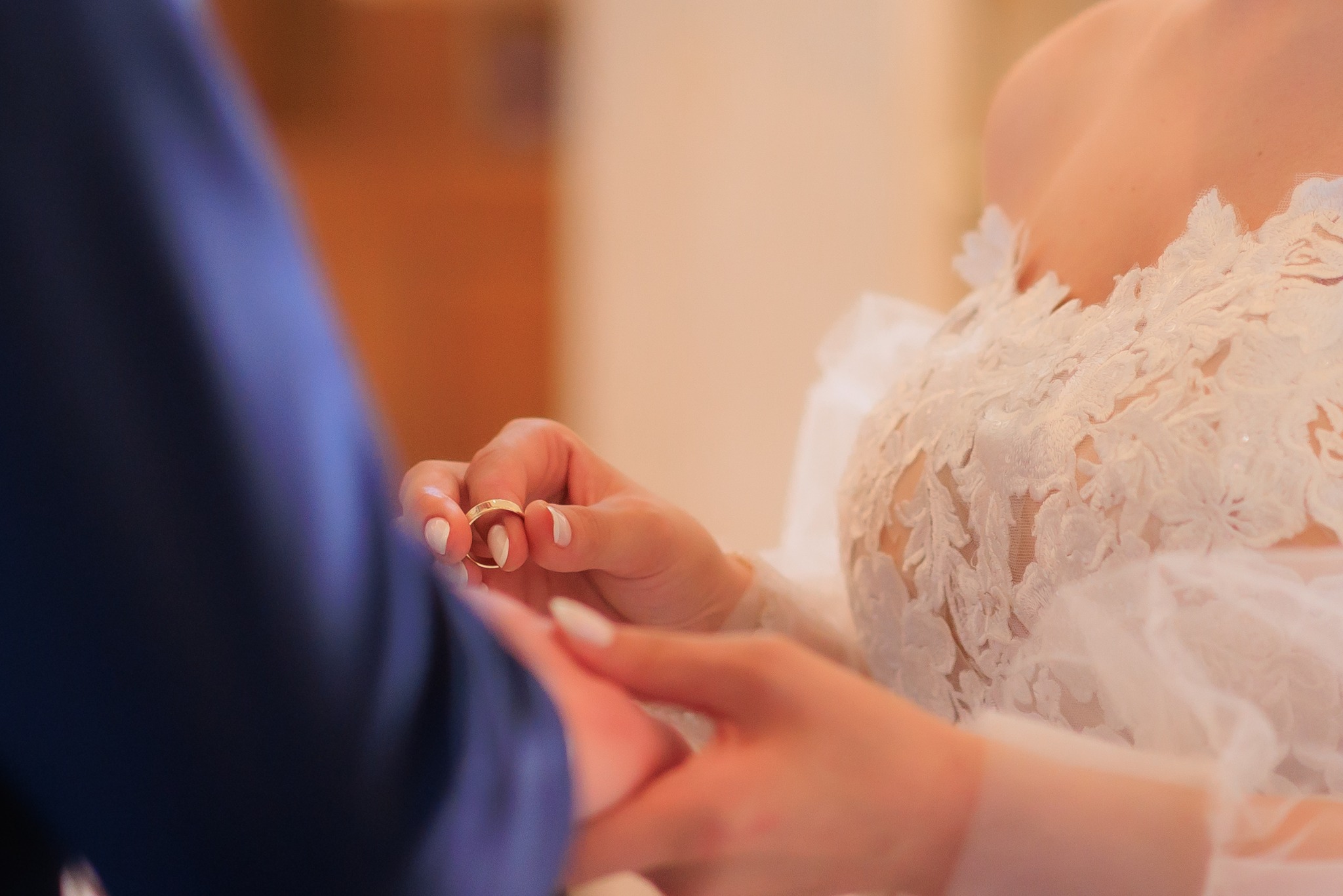 Dłonie Panny Młodej w koronkowej sukni trzymające obrączki ślubne, zbliżenie na delikatne dłonie i złote krążki.