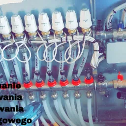 Rozdzielacz ogrzewania podłogowego z głowicami termostatycznymi Eberle, widoczne rury doprowadzające do poszczególnych pomieszczeń, narzędzie w tle sugeruje trwający montaż.