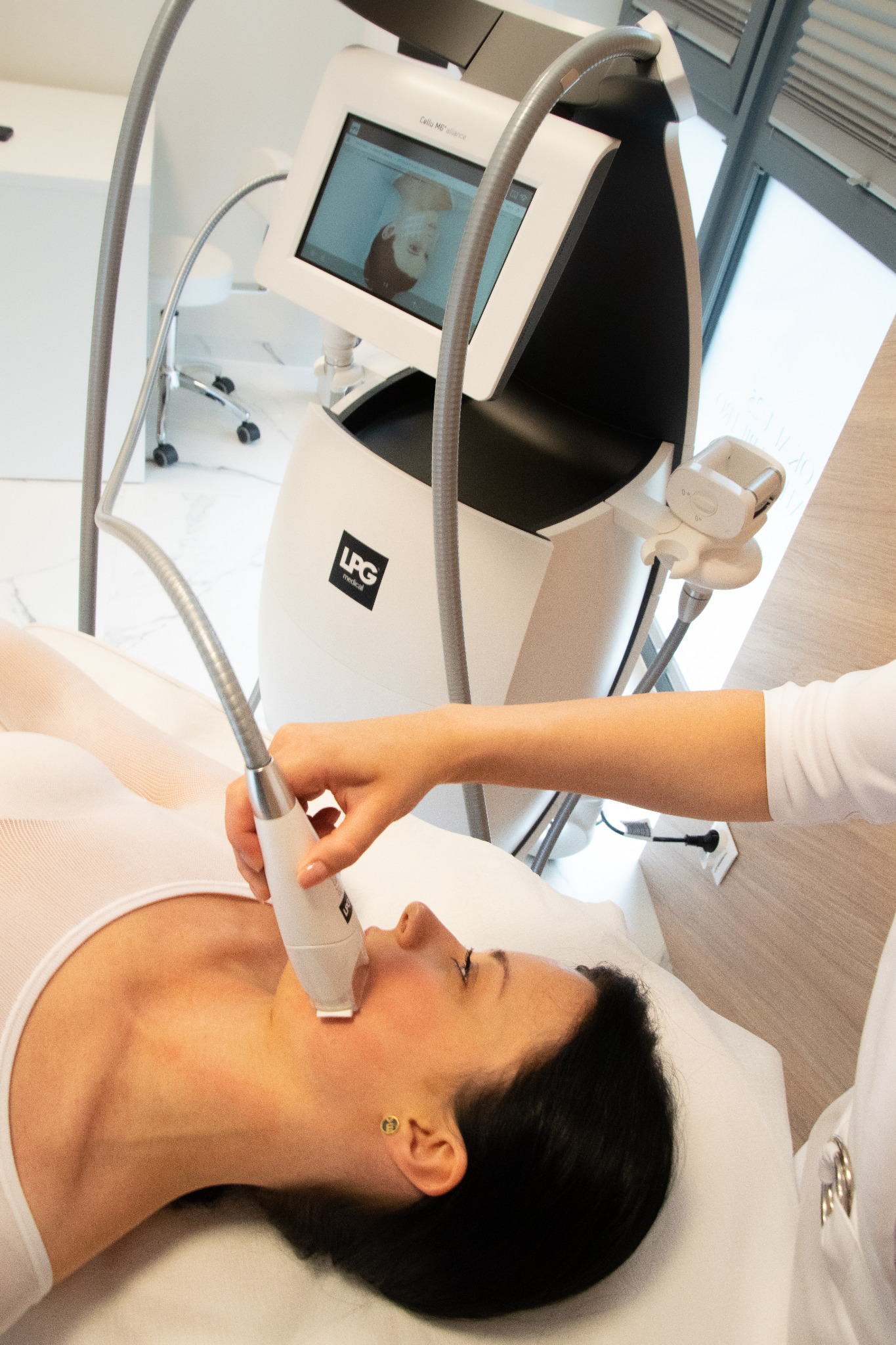 Kobieta poddawana zabiegowi na szyję przy użyciu urządzenia LPG Cellu M6 Alliance, widoczny ekran urządzenia z podglądem, złote kolczyki w uszach pacjentki.