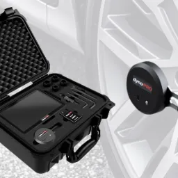 Zestaw diagnostyczny do pomiaru mocy silnika, umieszczony w otwartej walizce z piankowym wypełnieniem, obok koła samochodowego z zamontowanym czujnikiem.