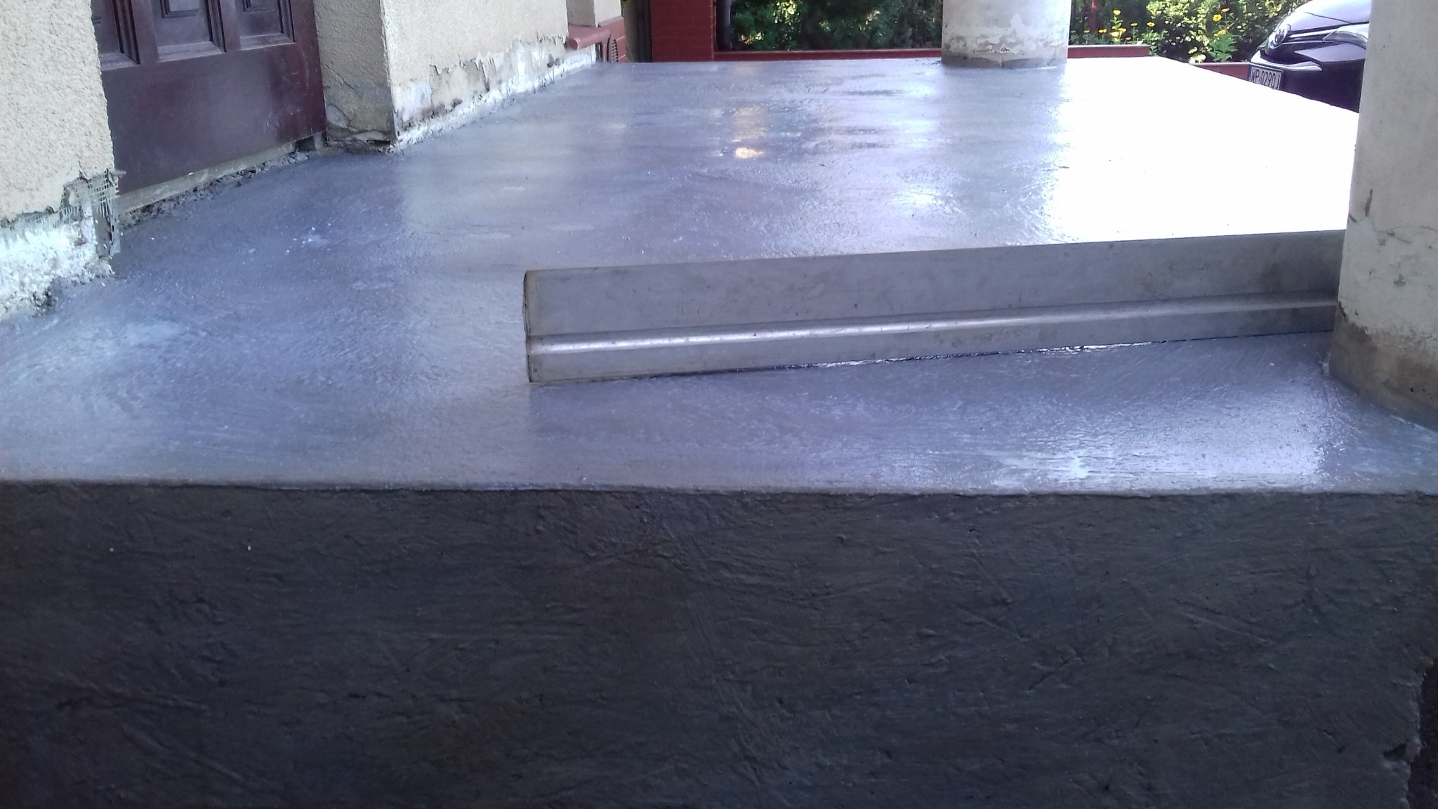 Wyrównywanie wylewki na betonowym tarasie przed wejściem do domu, widoczna poziomica i świeżo wylana, mokra powierzchnia.