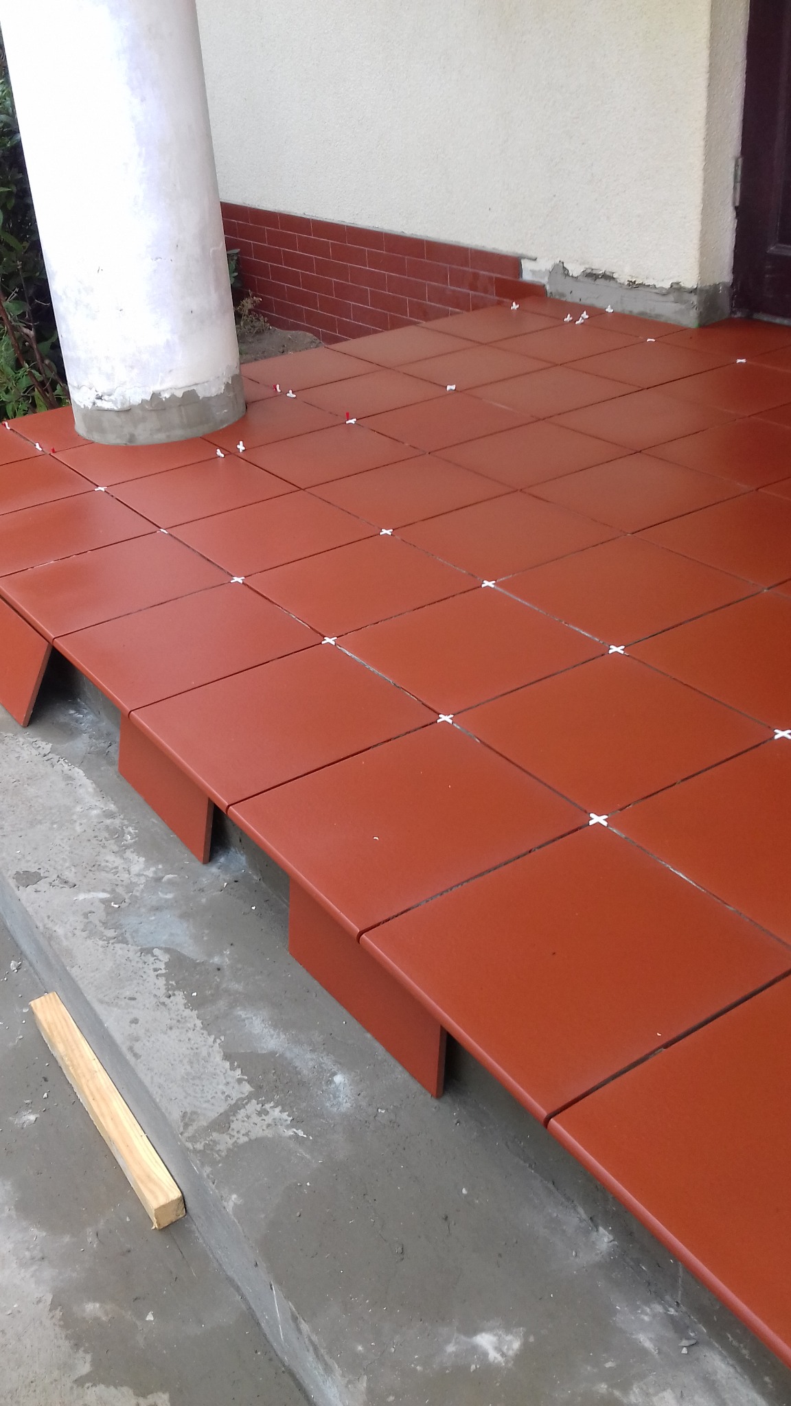 Układanie terakoty na zewnątrz budynku, widoczne krzyżyki dystansowe i fragment kolumny.