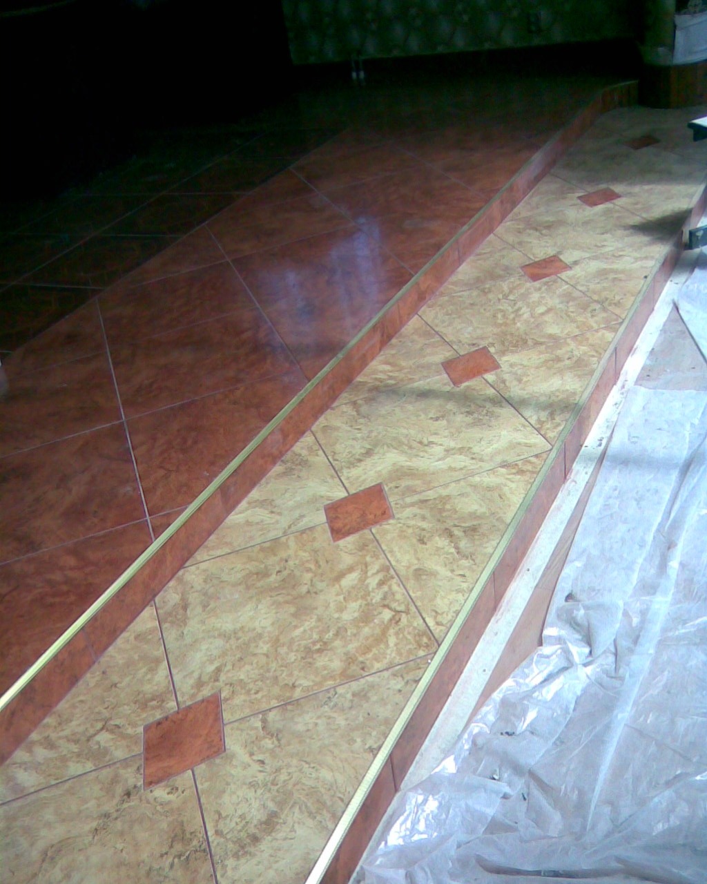 Wykończone schody wewnętrzne z brązowych płytek ceramicznych z dekoracyjnymi wstawkami, zabezpieczone folią ochronną podczas prac.