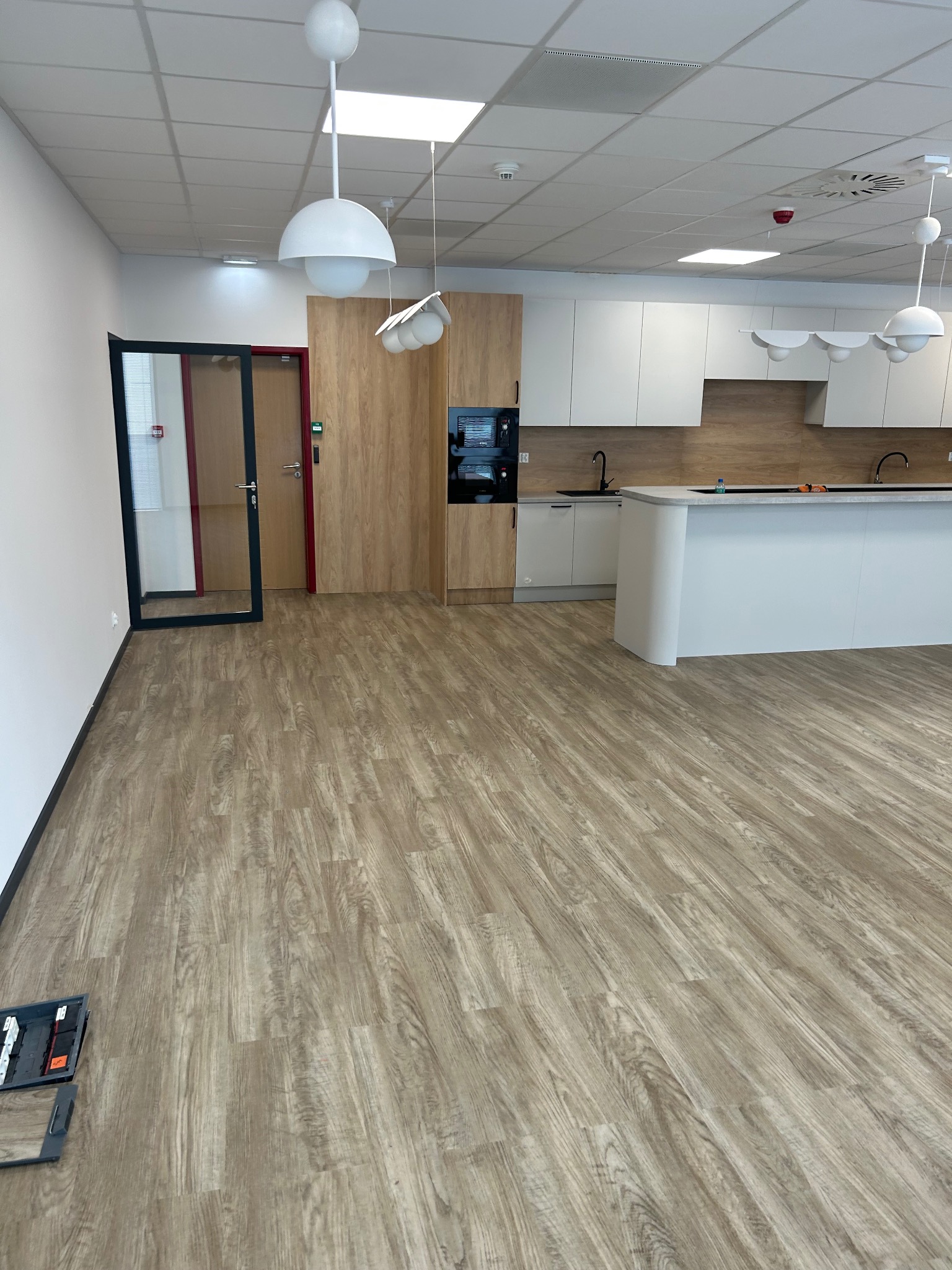 Jasne panele podłogowe w nowym biurze z aneksem kuchennym. Widoczne narzędzia do montażu paneli w lewym dolnym rogu.