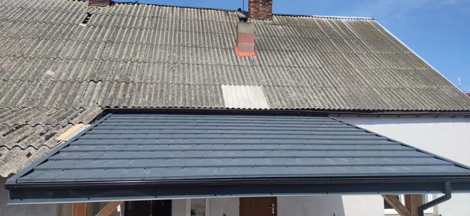 Fragment dachu z szarej blachy trapezowej, widoczny na tle starego dachu z szarego eternitu z kominem.