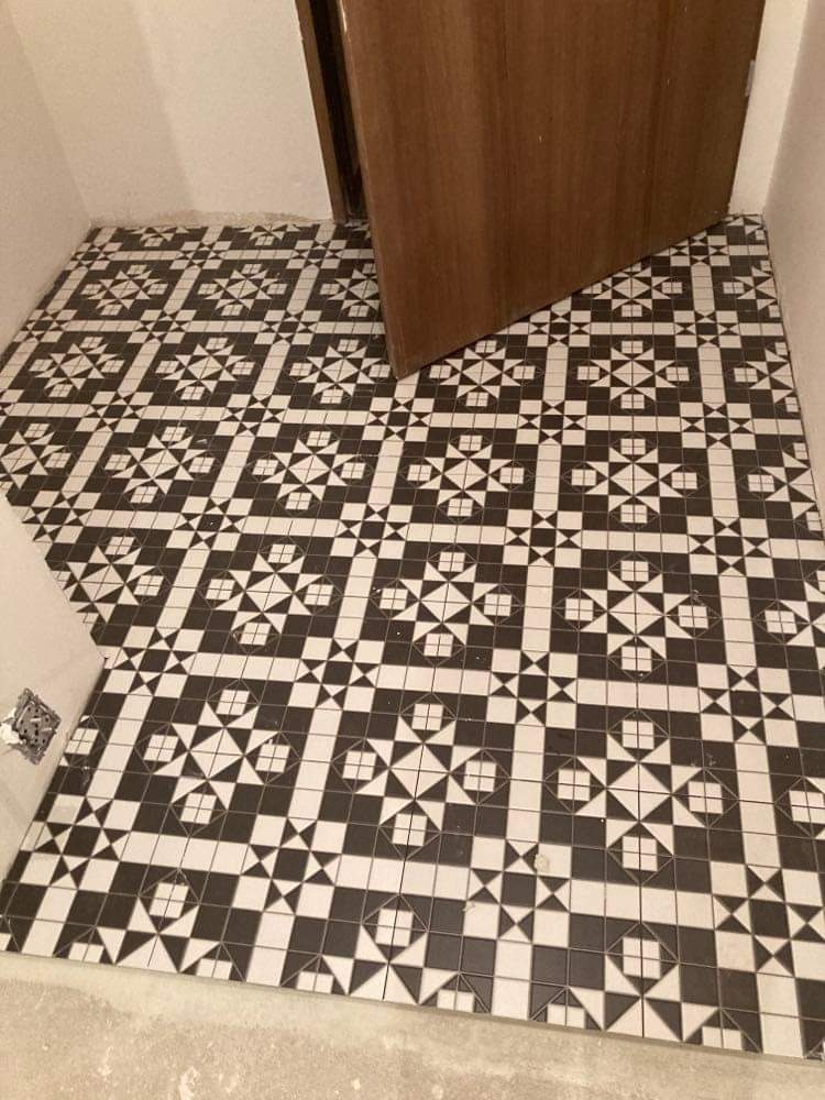 Ułożona podłoga z czarno-białych płytek o geometrycznym wzorze, widoczny fragment otwartych drzwi i niedokończone wykończenie ściany.