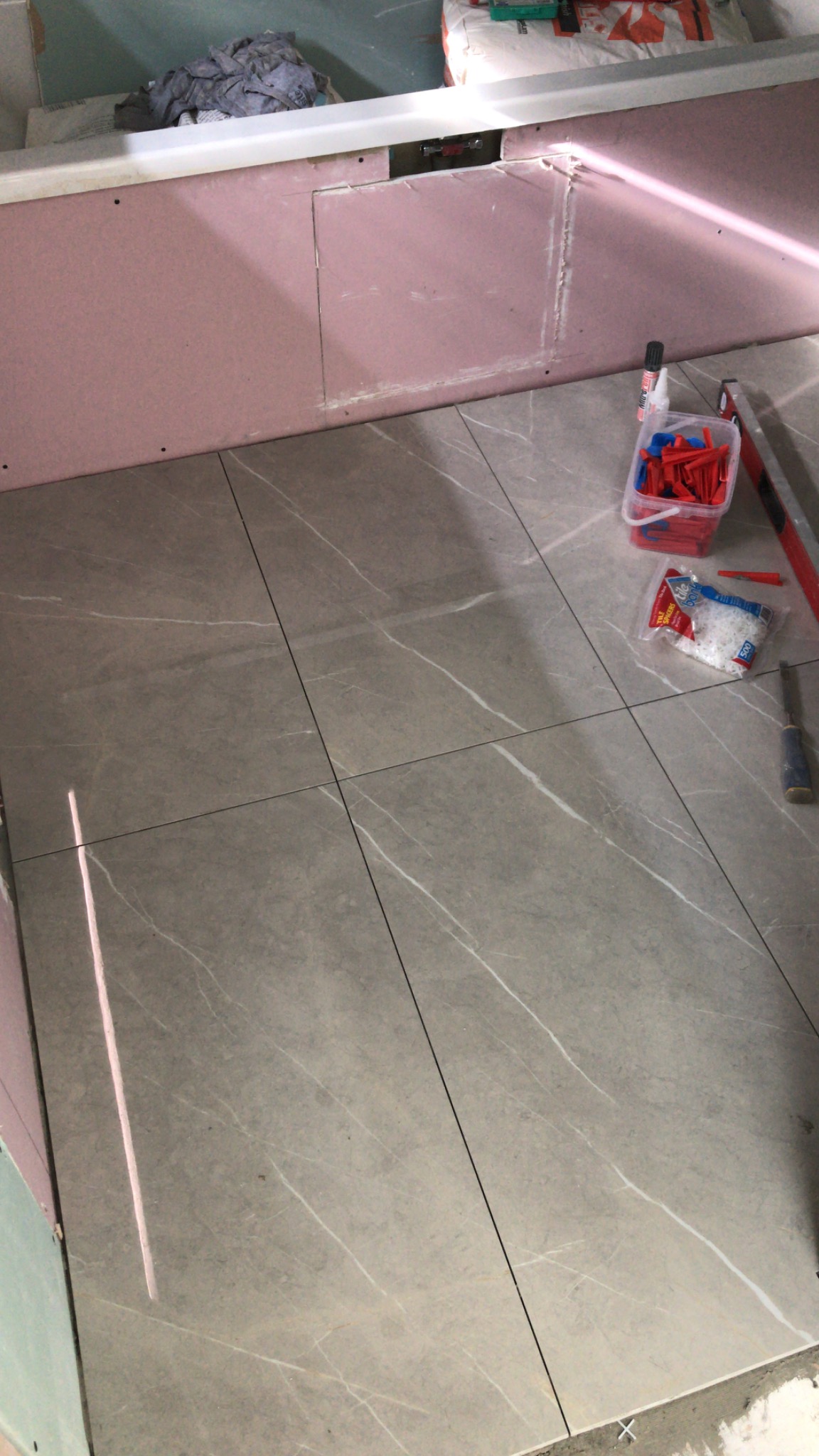 Układanie płytek imitujących marmur w łazience, widoczne narzędzia glazurnicze, ściany przygotowane pod dalsze prace wykończeniowe, brak fugowania.