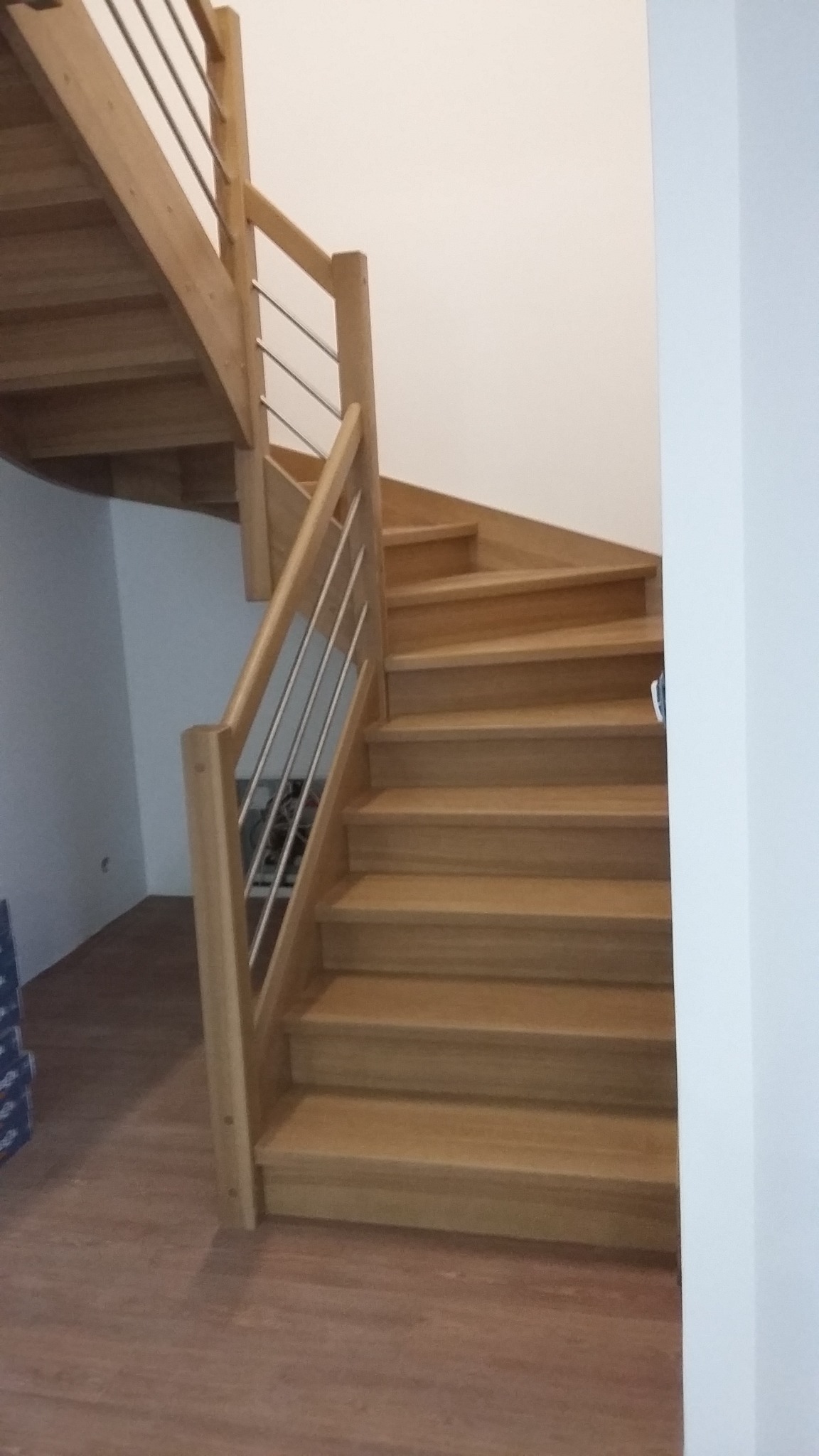 Jasne drewniane schody z metalowymi balustradami w nowoczesnym wnętrzu, widok z dołu, naturalne oświetlenie.