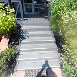 Stanisław kulik - Schody z deski kompozytowej prowadzące do domu, otoczone zielenią. Widoczny fragment tarasu i wejścia do budynku.