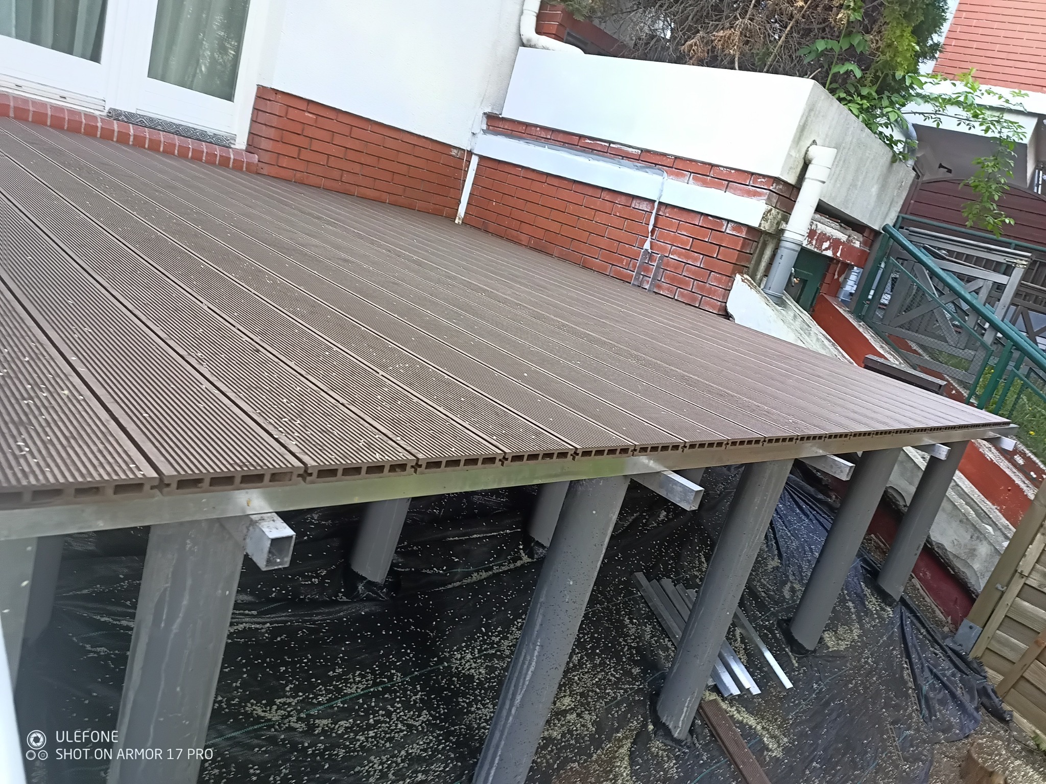 Nowoczesny taras kompozytowy w trakcie montażu, widoczne podpory i deski tarasowe. Ujęcie z dołu ukazuje konstrukcję nośną tarasu.