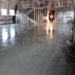 Wnętrze hali z polerowaną, szarą posadzką. Widoczna maszyna do polerowania podłóg Kreher oraz odbicia okien w błyszczącej powierzchni.