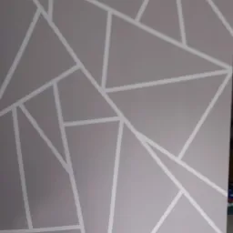 Ściana w odcieniach szarości z geometrycznym wzorem z białych linii, tworzących trójkąty i inne wielokąty.