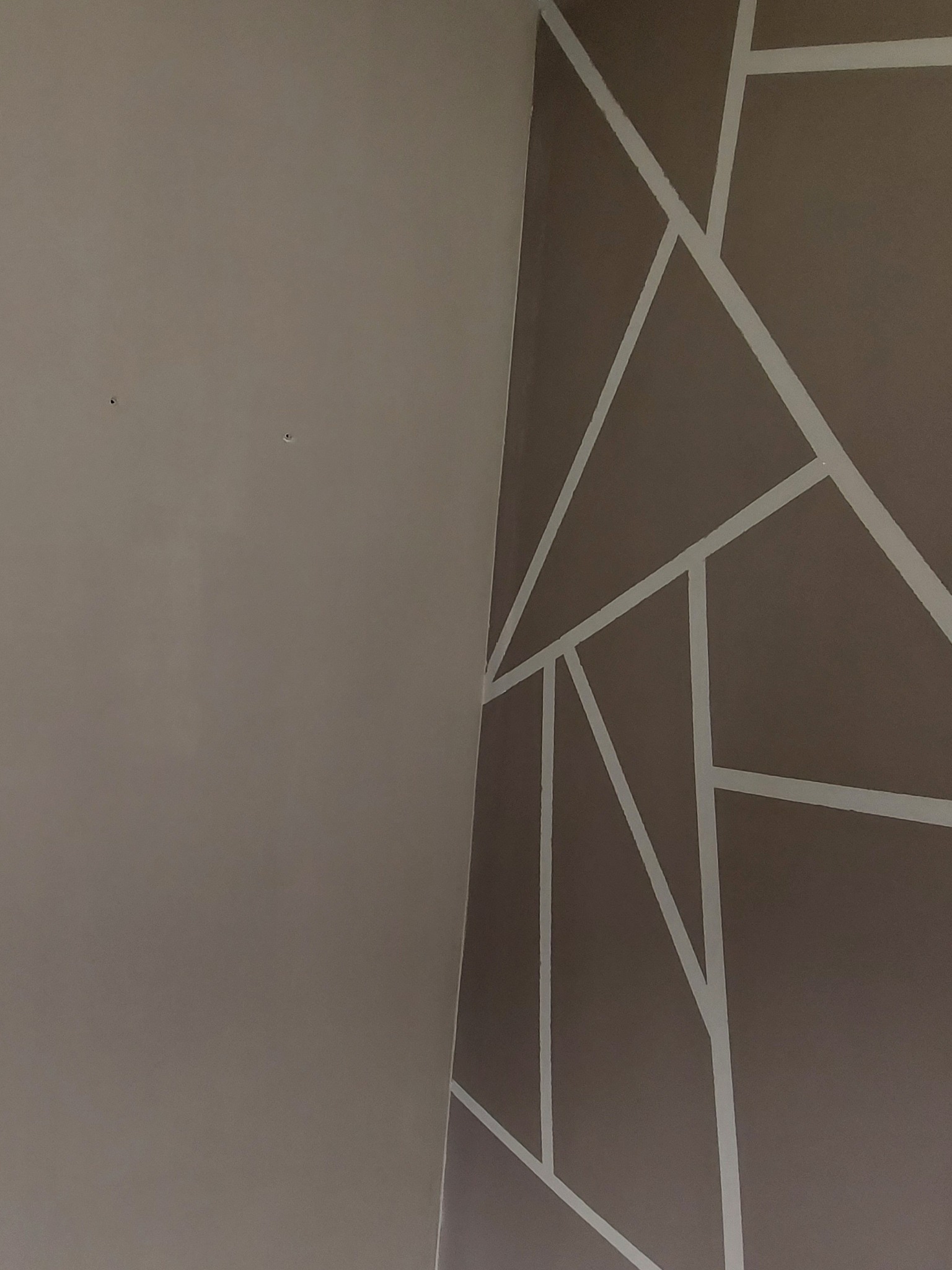 Fragment ściany z geometrycznym wzorem w odcieniach brązu i bieli, widoczne łączenie ściany z sufitem.