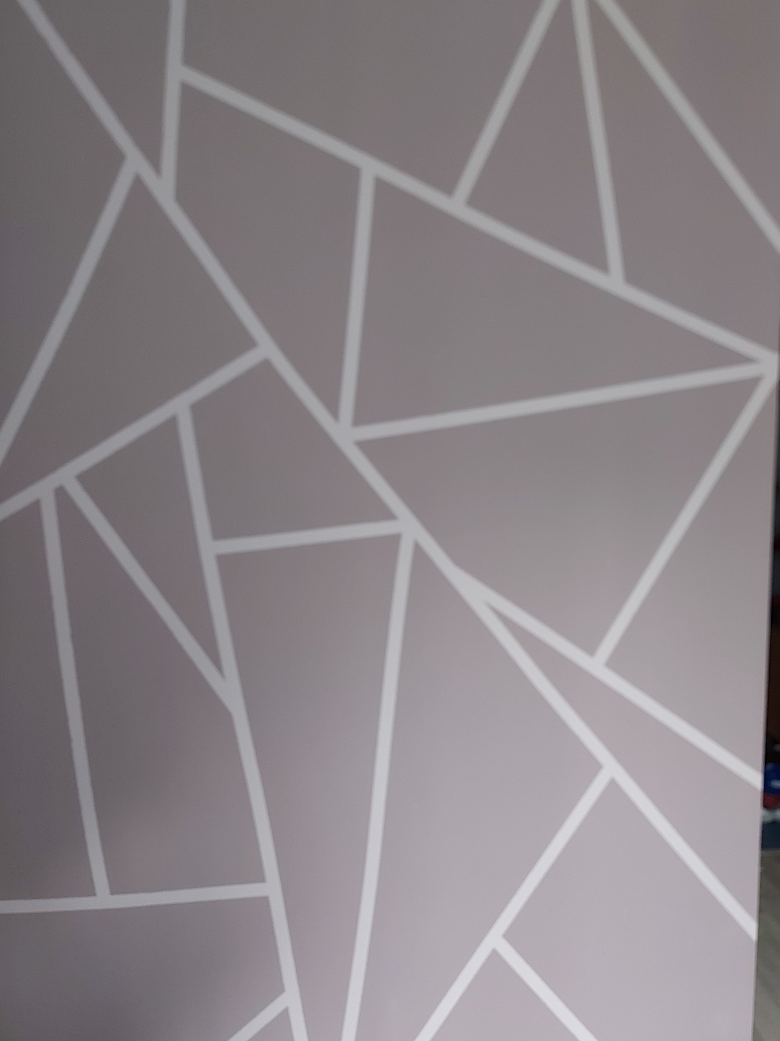 Ściana w odcieniach szarości z geometrycznym wzorem z białych linii, tworzących trójkąty i inne wielokąty.