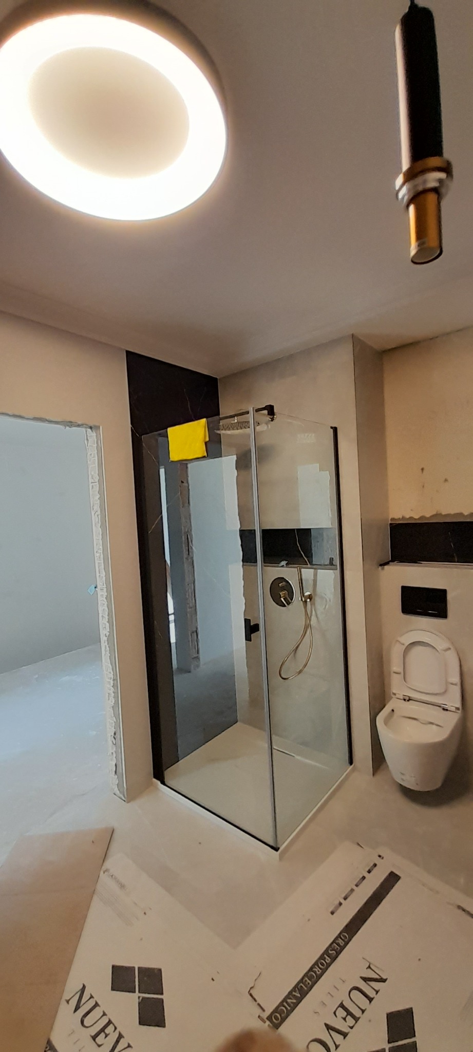 Nowoczesna kabina prysznicowa z czarnymi akcentami w łazience w trakcie remontu, widoczne płyty podłogowe z logo 'NUEVO TILES'