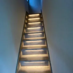 Schody z podświetleniem LED wzdłuż stopni, widok z dołu, ściany pomalowane na szaro.