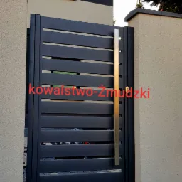 Nowoczesna brama wjazdowa z poziomymi panelami w kolorze antracytowym, z pionowym, metalowym uchwytem, zamontowana pomiędzy dwoma filarami z jasnego piaskowca, widok z zewnątrz na kostkę brukową.