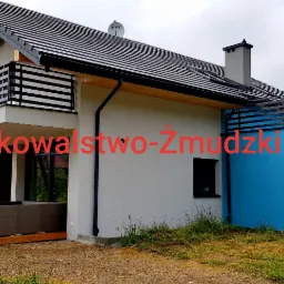 Nowoczesny dom jednorodzinny z płaskim dachem i czarnymi balustradami poziomymi na balkonie i tarasie, widok z boku na tle pochmurnego nieba.