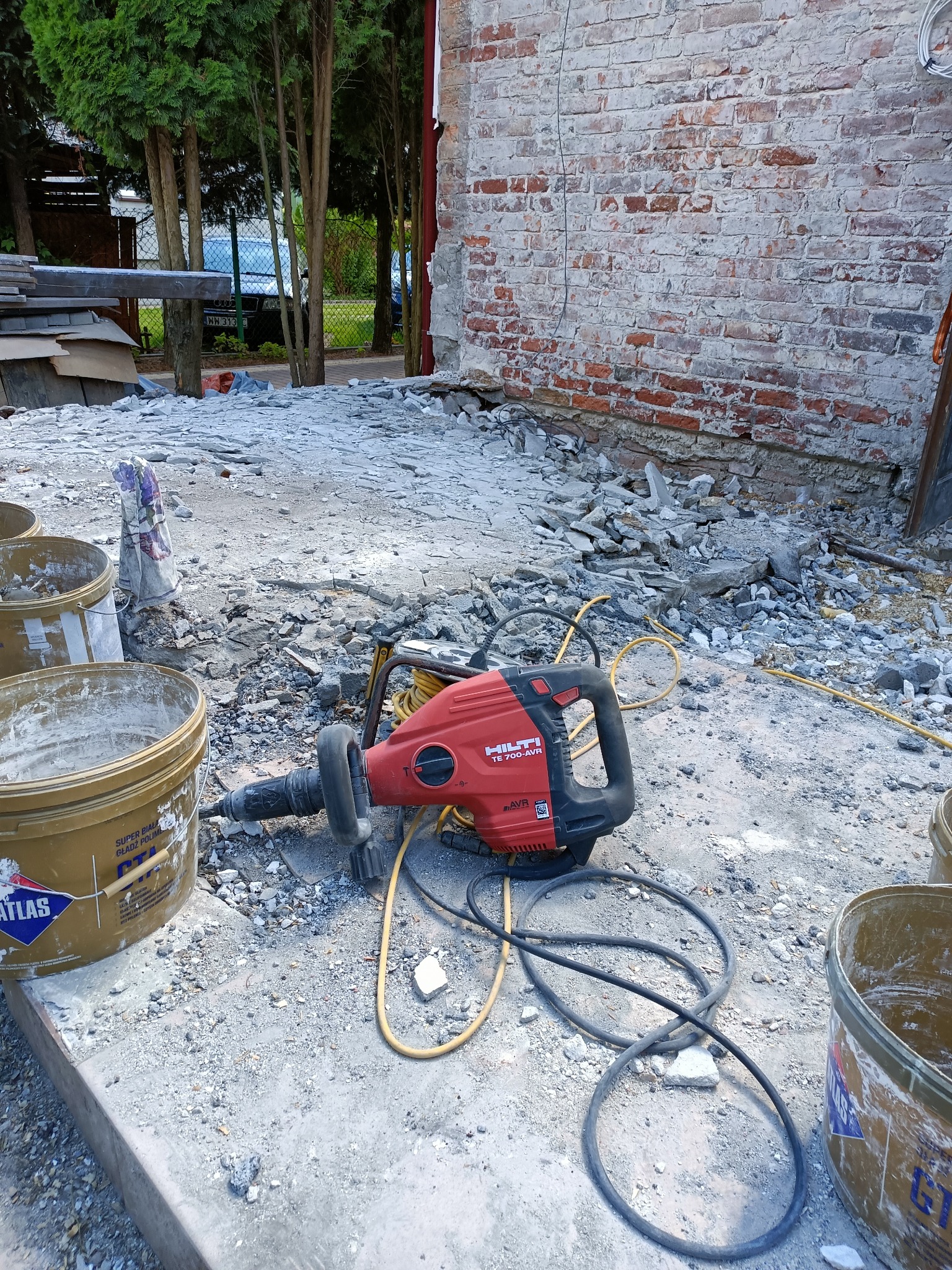 Czerwony młot udarowy Hilti TE 700-AVR leży na gruzie obok wiaderek z resztkami zaprawy murarskiej, przy ceglanej ścianie w trakcie prac remontowych.