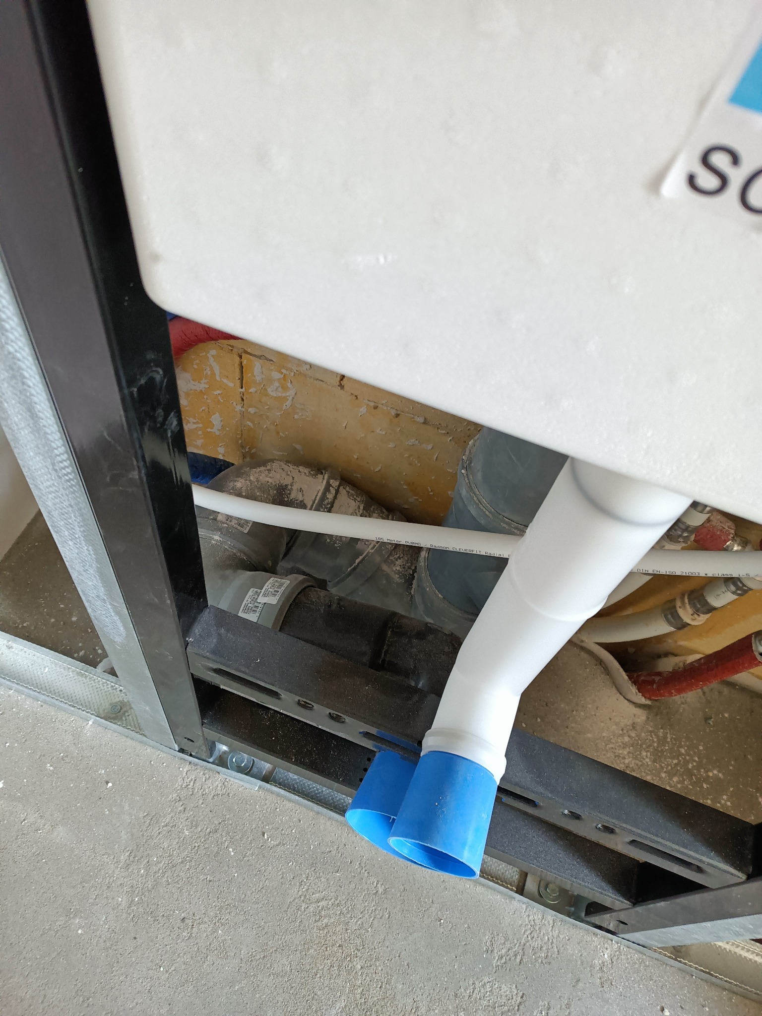 Stelaż podtynkowy WC z widocznymi rurami kanalizacyjnymi i instalacją wodną, przed zabudową płytą karton-gips.