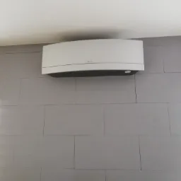 Biała jednostka klimatyzacyjna Daikin zamontowana na szarej ścianie z płytek w pomieszczeniu.