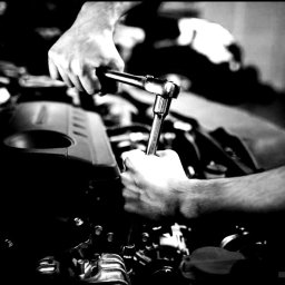 Automechanika Ratka DDCars - Czarno-białe zdjęcie mechanika dokręcającego śrubę w silniku samochodowym za pomocą klucza nasadowego z grzechotką.