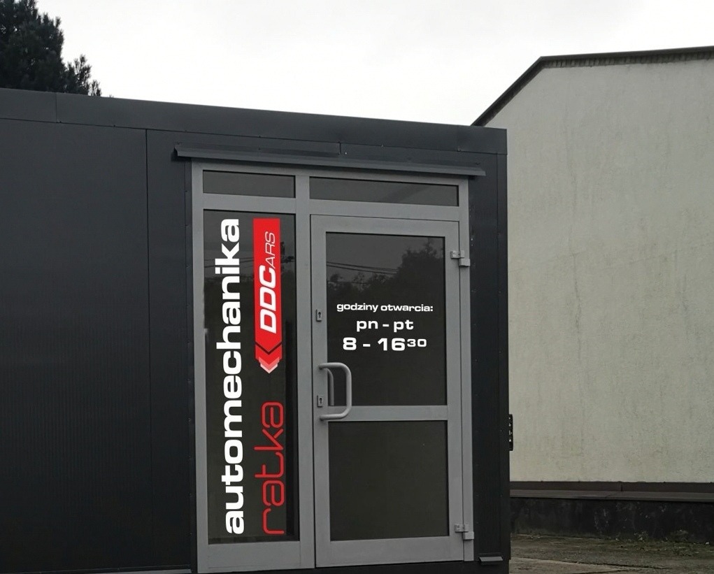 Wejście do warsztatu samochodowego z logo 'automechanika ratka DDCARS' na drzwiach i godzinami otwarcia pn-pt 8-16:30.