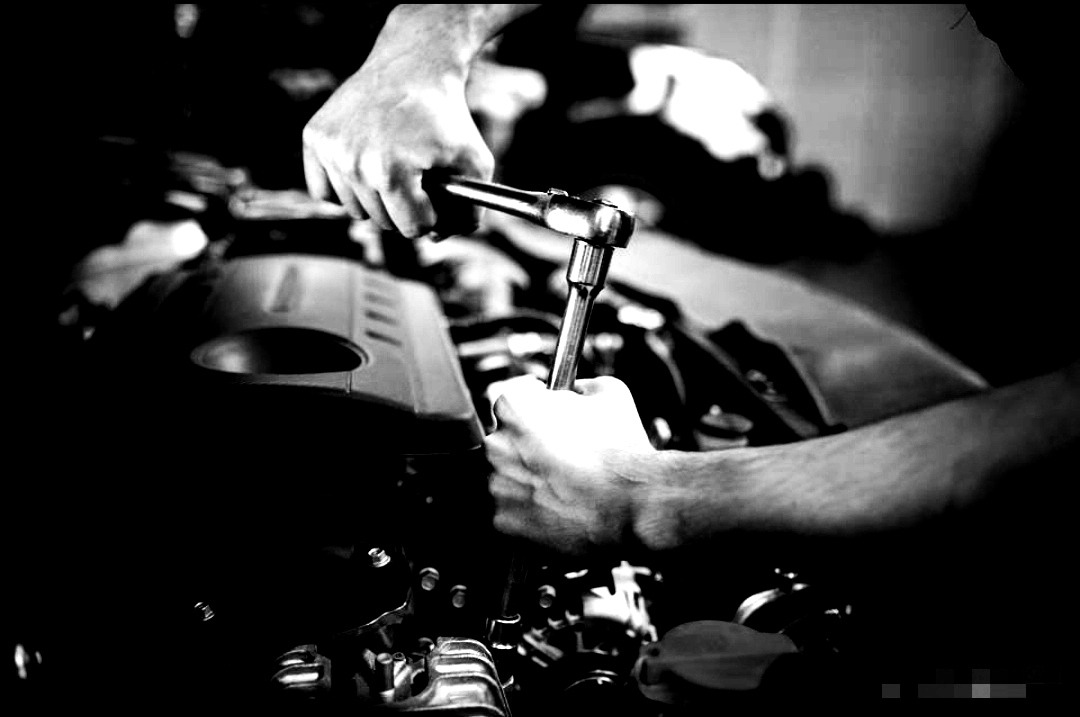 Czarno-białe zdjęcie mechanika dokręcającego śrubę w silniku samochodowym za pomocą klucza nasadowego z grzechotką.