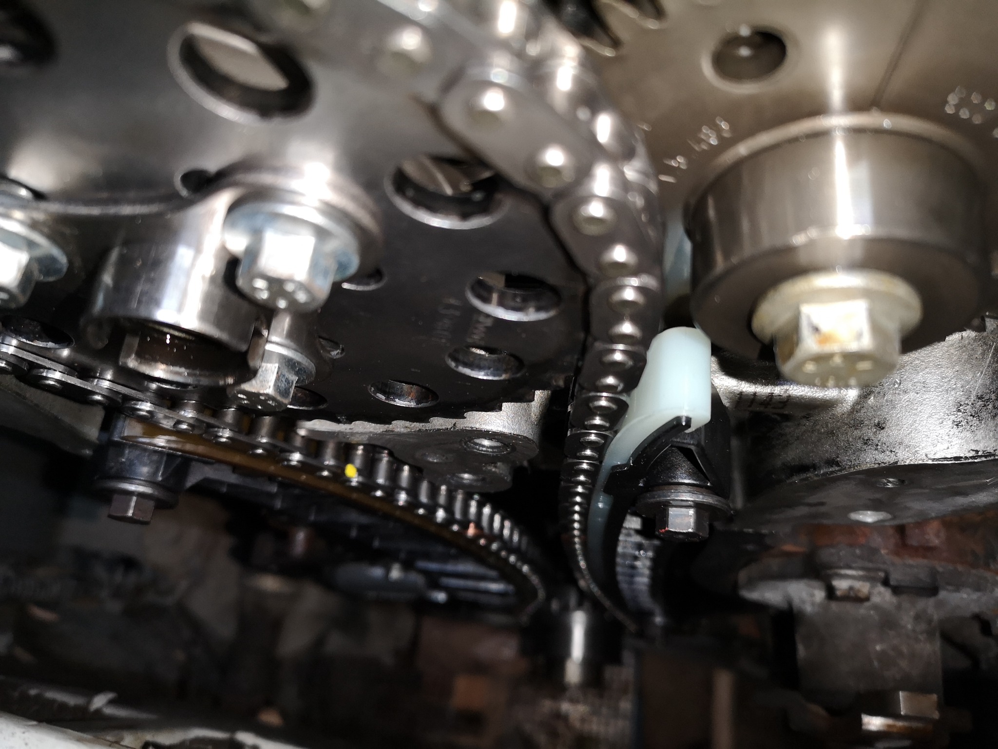 Metalowe koła zębate i łańcuch rozrządu w silniku samochodowym, widoczne ślady oleju, perspektywa od dołu.