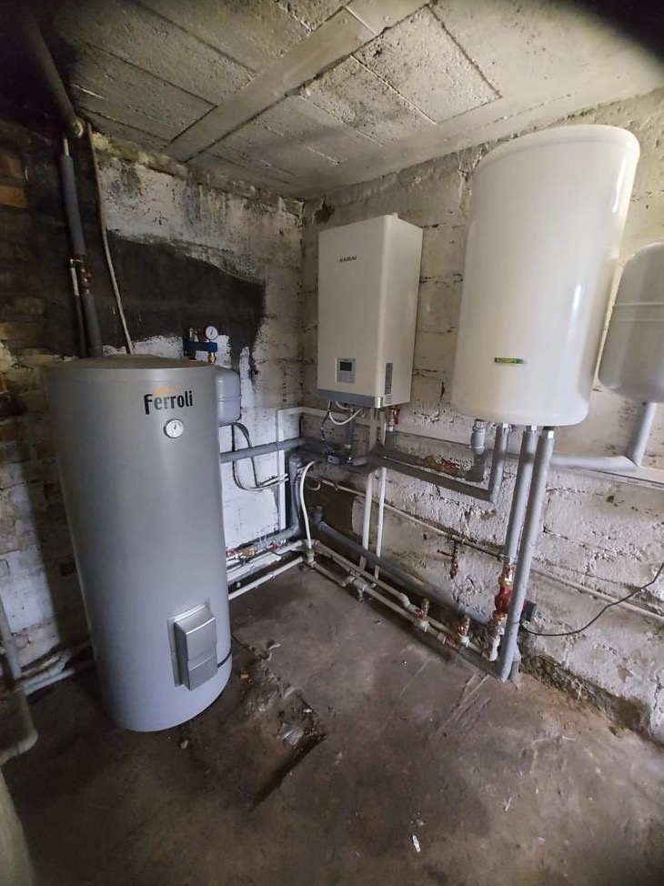 Instalacja pompy ciepła marki Ferroli i Kaisai w piwnicy w Poznaniu, widoczne rury i zasobnik ciepłej wody.