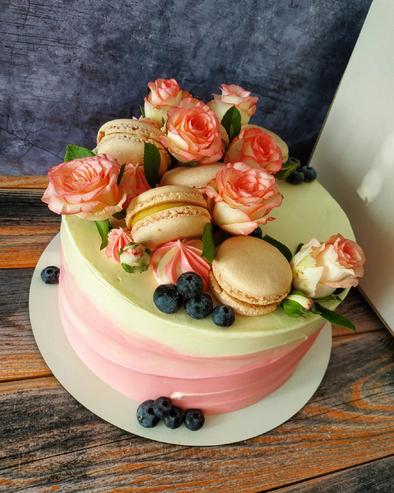 Tort ombre w odcieniach różu i kremu, udekorowany świeżymi różami z delikatnym różowym obrzeżem, beżowymi makaronikami z żółtym kremem i świeżymi borówkami.