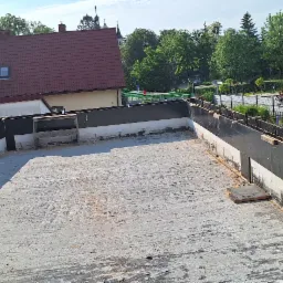 Przygotowany betonowy dach płaski z czarnym szalunkiem i drewnianymi podporami, widok z góry na tle zabudowy miejskiej.