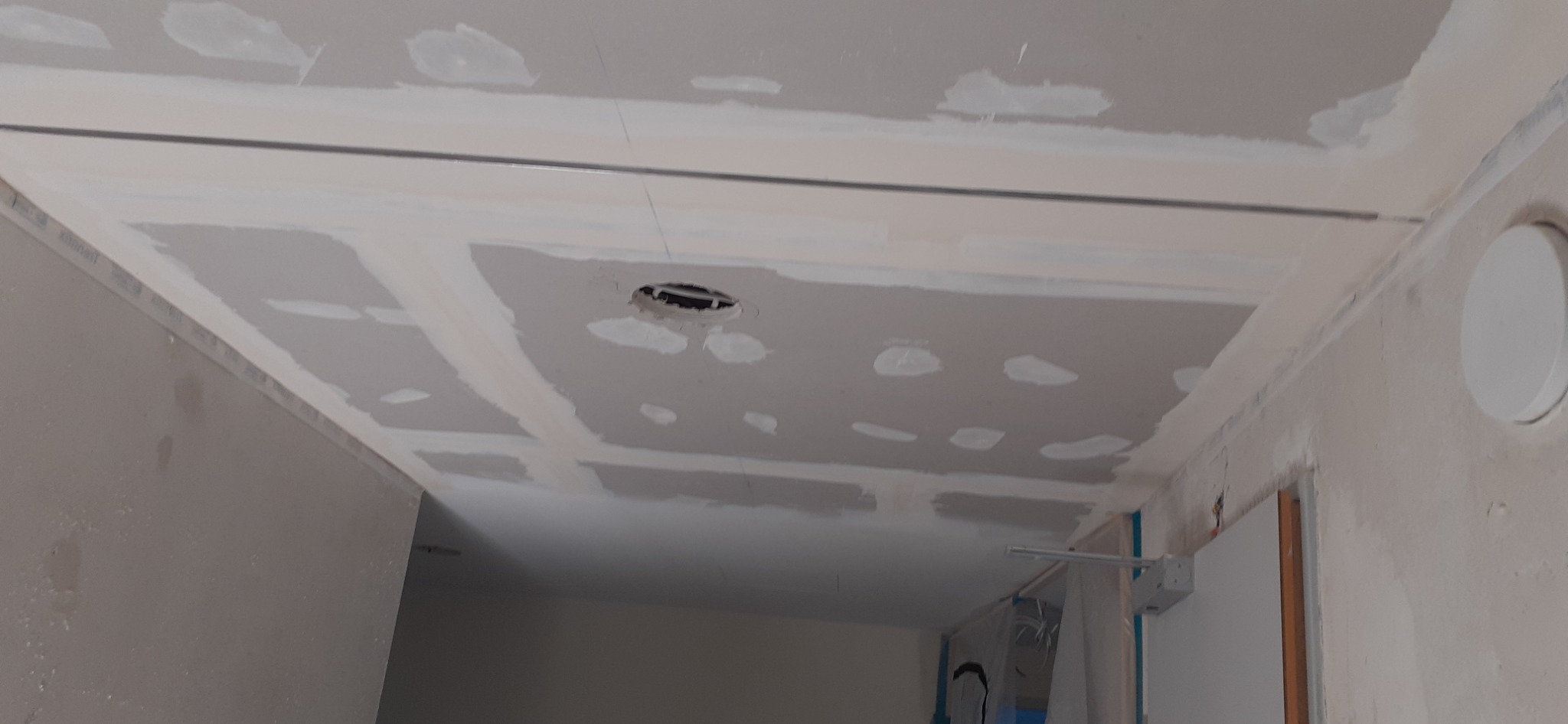 Sufit podwieszany z płyt gipsowo-kartonowych w trakcie montażu, widoczne łączenia i otwór na oświetlenie, surowy stan wykończenia ścian.