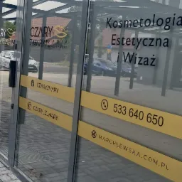 Szklane drzwi wejściowe do salonu z napisem 'Kosmetologia Estetyczna i Wizaż', logo firmy 'Czary Zmary Maria Marchlewska', danymi kontaktowymi i adresami w mediach społecznościowych na żółtych pasach.