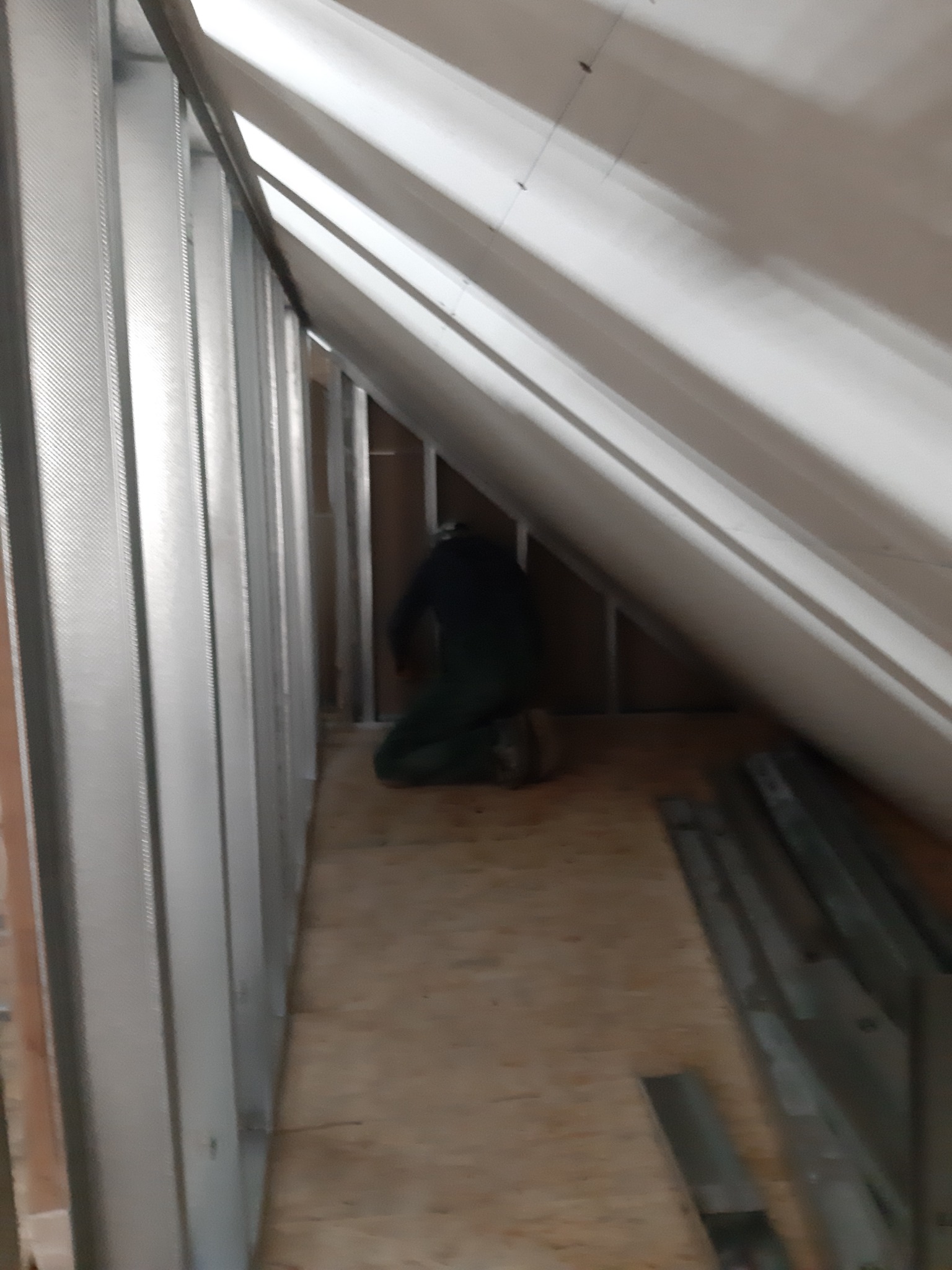 Prace wykończeniowe na poddaszu: montaż metalowego stelażu pod płyty gipsowo-kartonowe, widoczna ukośna konstrukcja dachu i pracownik w trakcie instalacji.