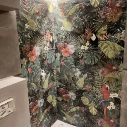 Wykończona ściana prysznicowa z dekoracyjnymi płytkami w tropikalny wzór z motywem papug, tukanów i bujnej roślinności, podświetlona od góry listwą LED.