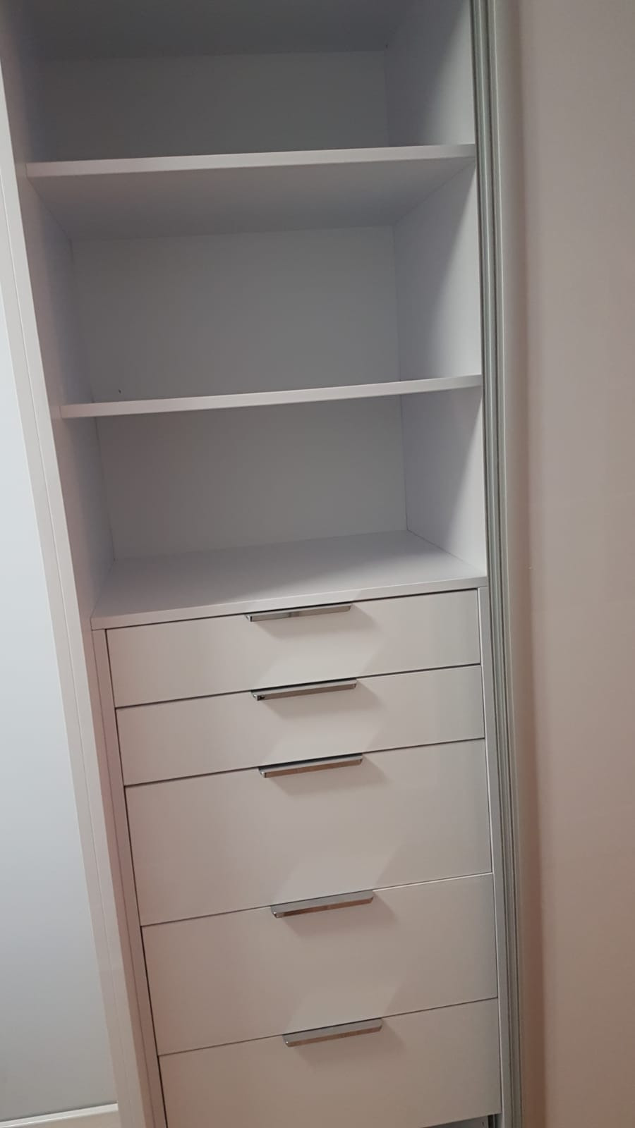 Wnętrze białej szafy wnękowej z czterema szufladami i półkami, widoczne metalowe uchwyty.