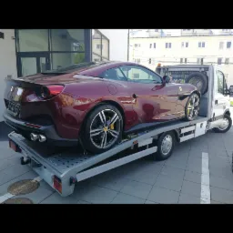 Czerwone Ferrari na platformie lawety, widok z tyłu, żółte zaciski hamulcowe, budynek w tle.