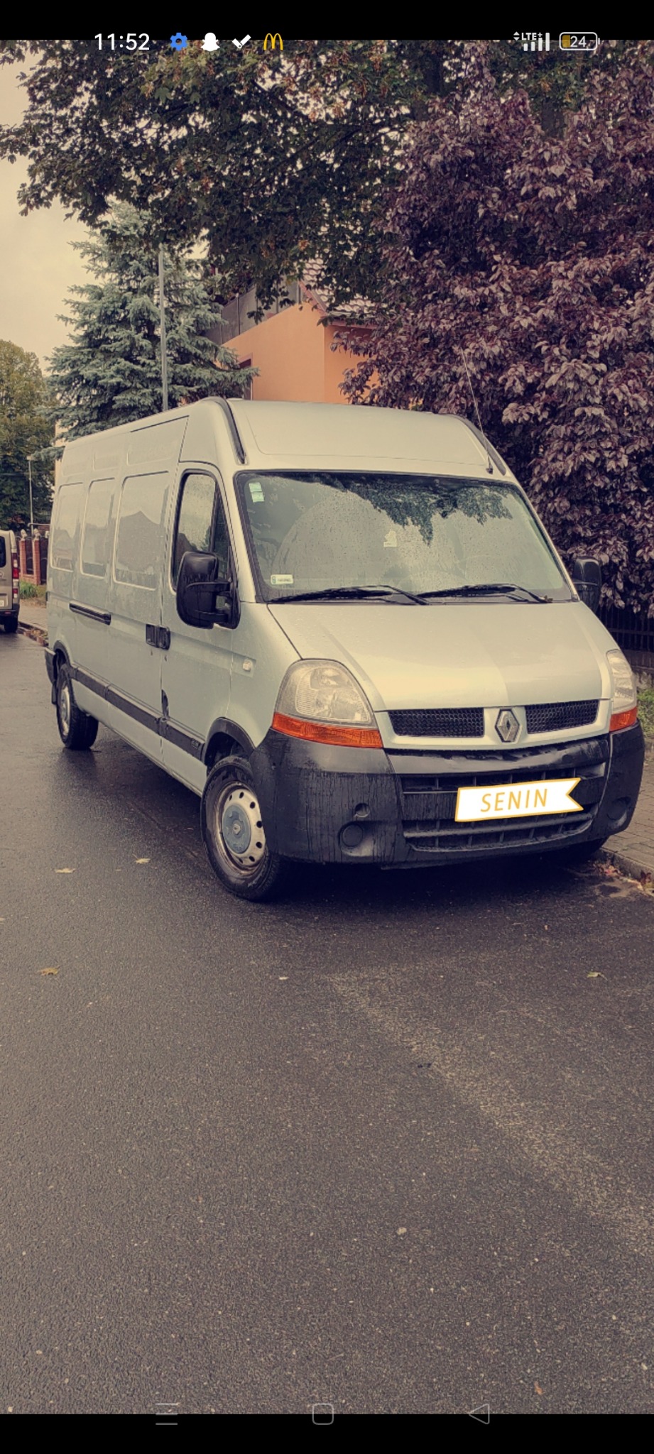 Srebrny Renault Master parkuje na mokrej ulicy, widoczne mokre ślady na karoserii i oponach, w tle drzewa i budynek.