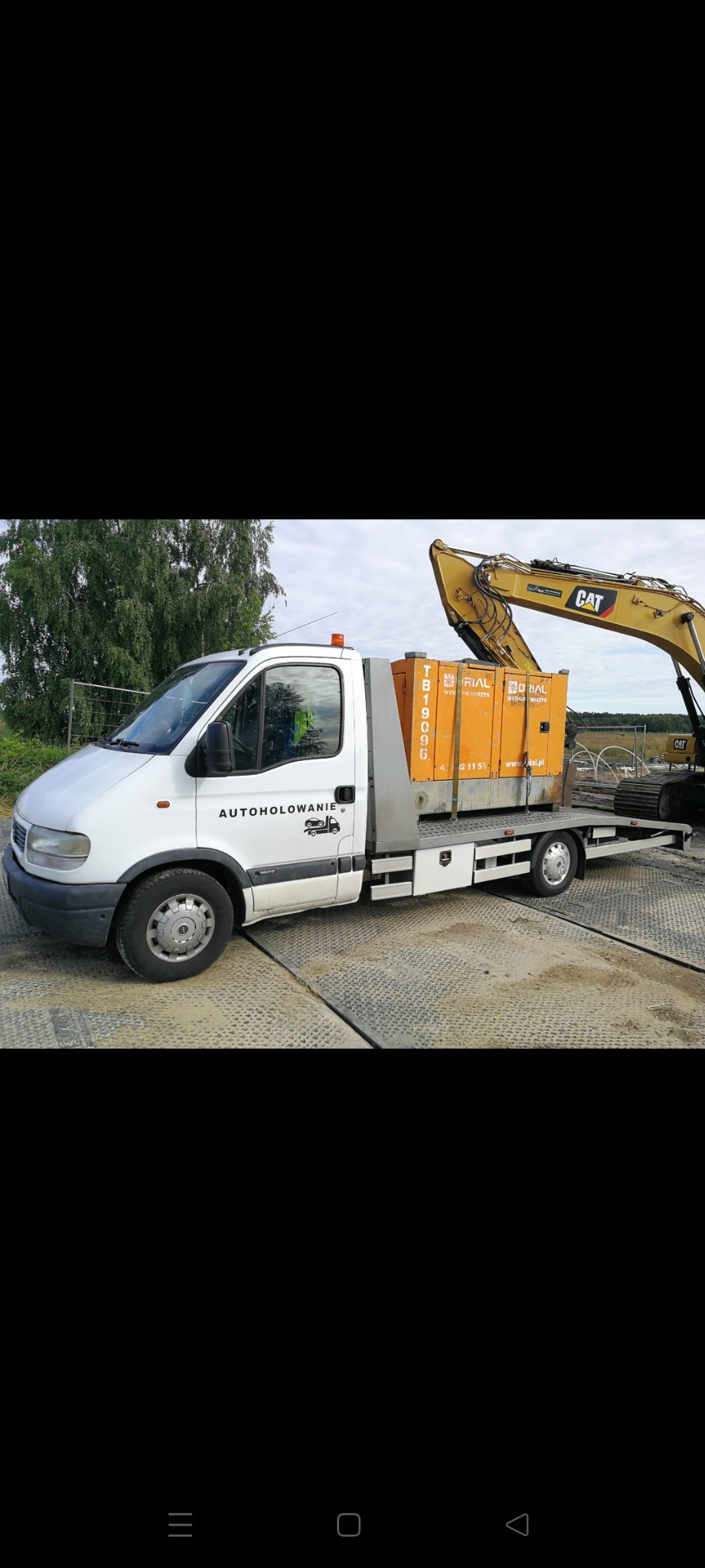 Biała laweta z napisem 'AUTOHOLOWANIE' przewozi pomarańczowe agregaty prądotwórcze marki RIAL, z tyłu widoczna koparka CAT na platformie.