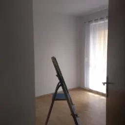 Pokój po odświeżeniu ścian, widoczna drabina malarska, białe ściany, drewniana podłoga i okno z białymi zasłonami.