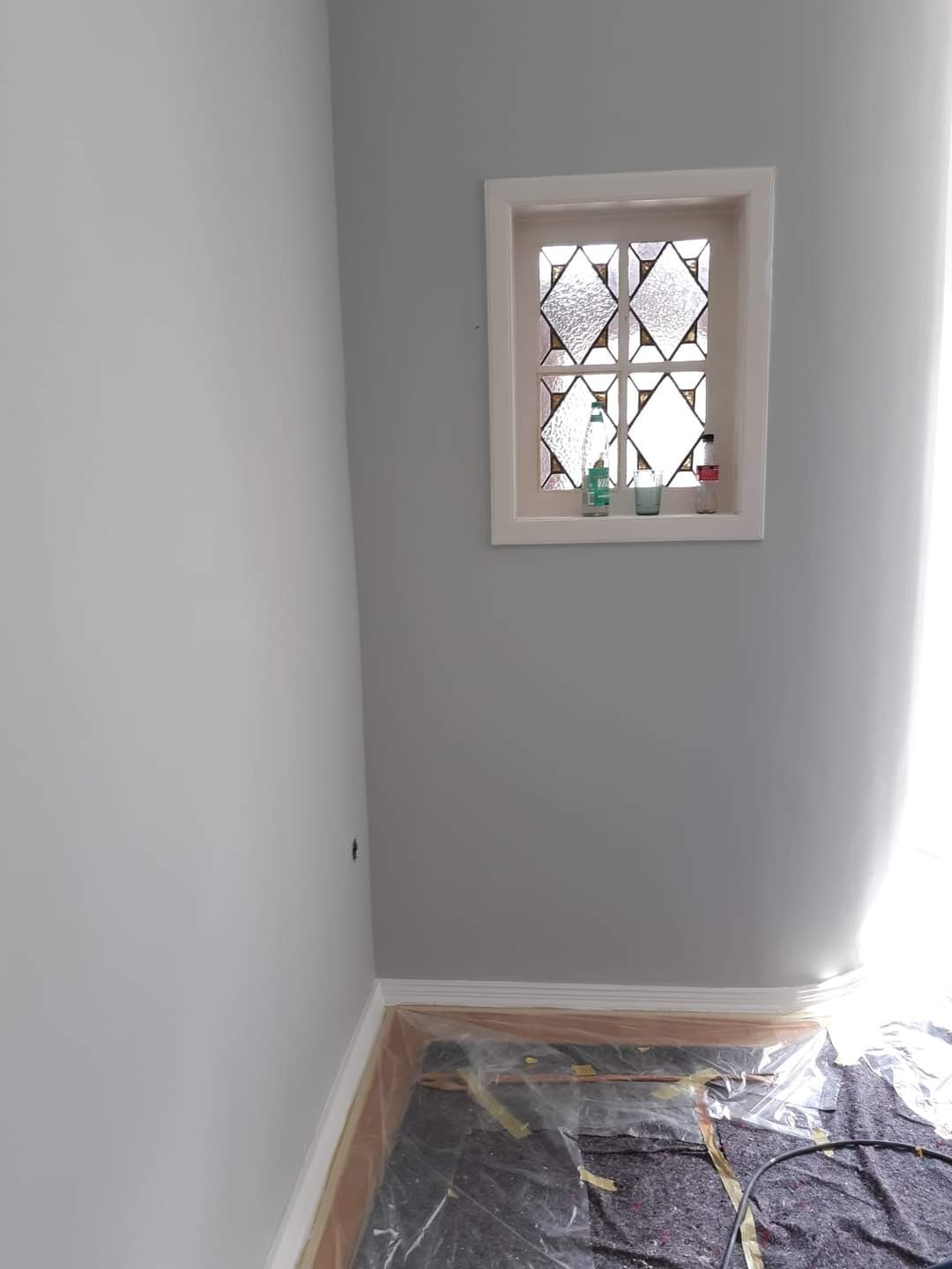 Świeżo pomalowane na szaro wnętrze pokoju z ozdobnym oknem, podłoga zabezpieczona folią malarską.