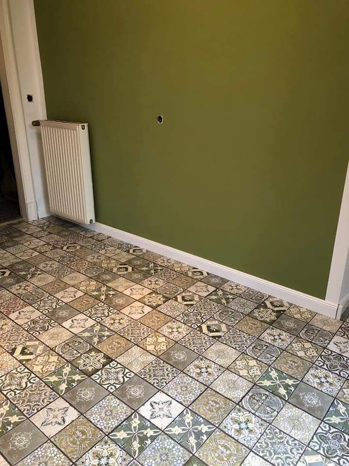 Wnętrze z zieloną ścianą i wzorzystą, ułożoną w karo podłogą z płytek ceramicznych w stylu vintage, biała listwa przypodłogowa i grzejnik żeberkowy.