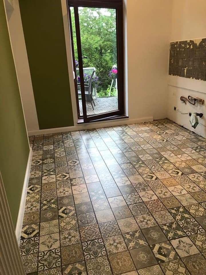 Nowo ułożona podłoga z wzorzystych, kwadratowych płytek w pomieszczeniu z zieloną ścianą i otwartym oknem balkonowym z widokiem na taras.