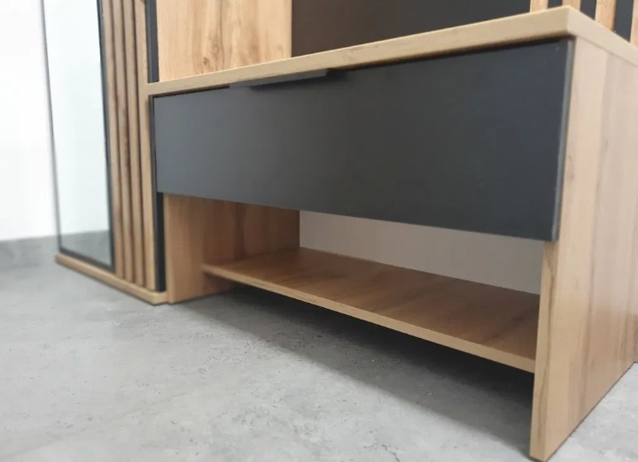 Fragment szafy z szufladą w kolorze grafitowym i półką, wykończona okleiną imitującą jasne drewno, z widocznymi pionowymi lamelami i elementem lustra.