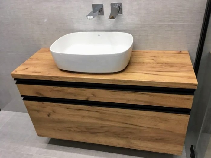 Nowoczesna łazienka z umywalką nablatową w kształcie kwadratu, osadzoną na szafce z drewnopodobnym fornirem i czarnymi akcentami, minimalistyczne baterie ścienne.