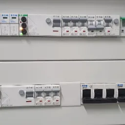 Rozdzielnica elektryczna Eaton z zabezpieczeniami nadprądowymi i różnicowoprądowymi, widoczne oznaczenia i parametry techniczne, zamontowana w szarej obudowie.