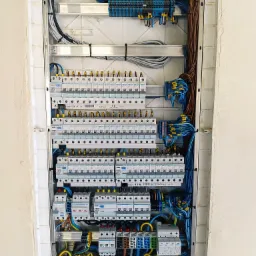 Rozdzielnica elektryczna z licznymi zabezpieczeniami, przewodami oznaczonymi tulejkami, zamontowana w ścianie w trakcie wykańczania.