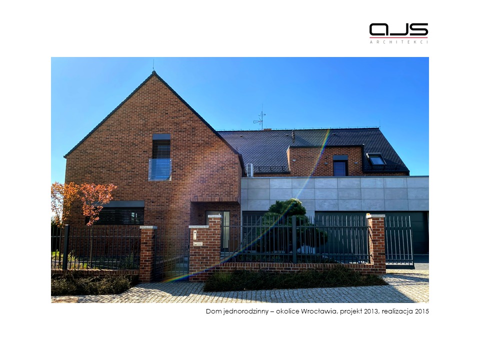 Nowoczesny dom jednorodzinny z cegły klinkierowej z elementami grafitowej elewacji, widoczny z poziomu chodnika przed ogrodzeniem.